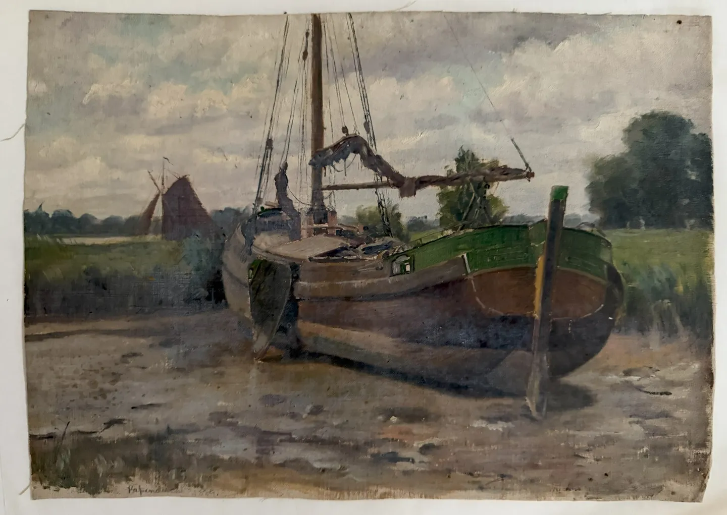 A wooden sailing barge resting on a muddy bank, a windmill and trees behind