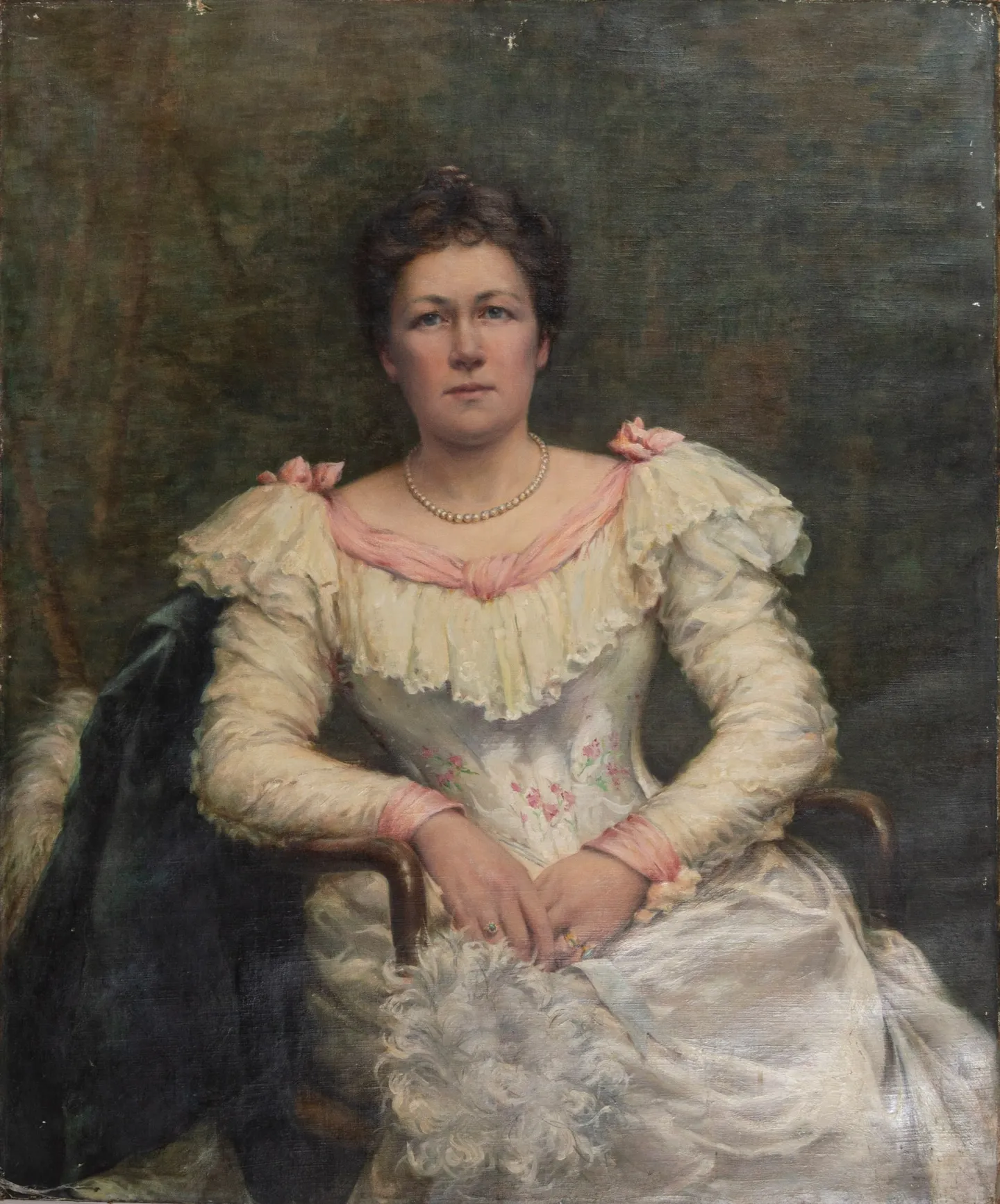 A woman in a white satin and lace gown, a dark wrap over her chair