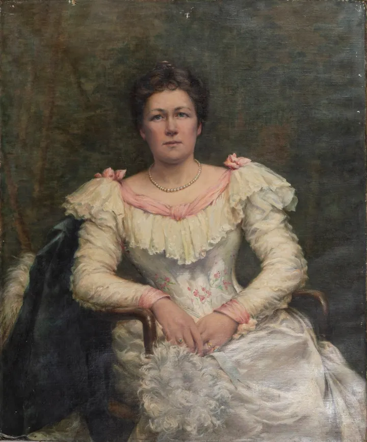 A woman in a white satin and lace gown, a dark wrap over her chair