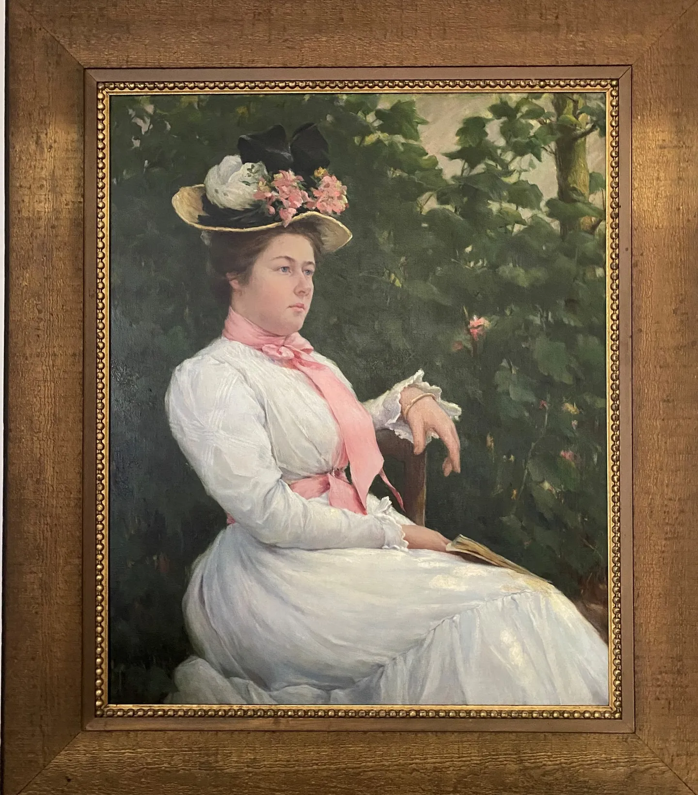 A young woman in a white dress and flowered hat seated in a garden