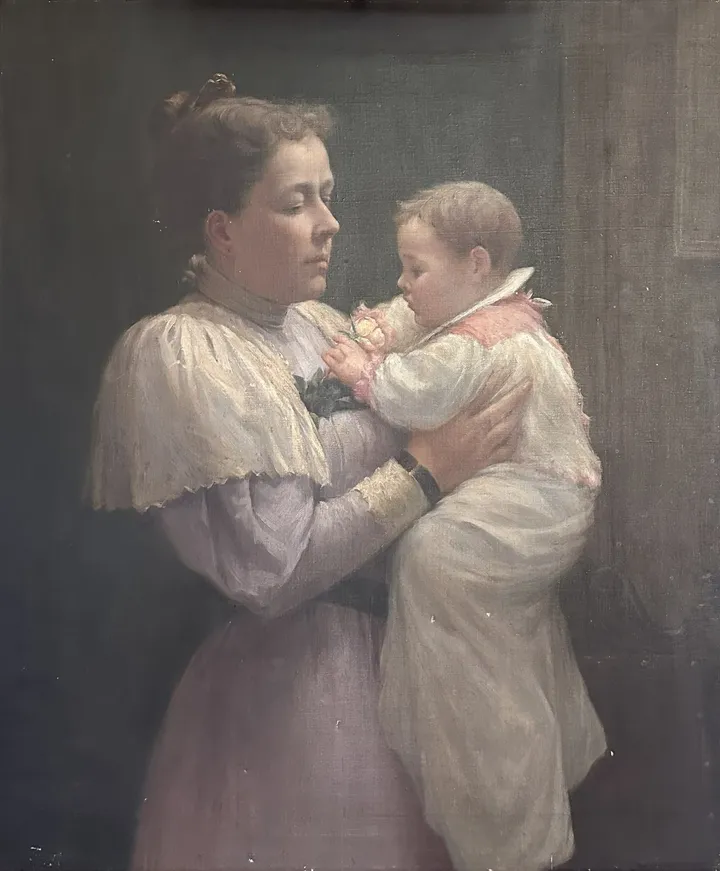 A mother in a lilac dress holds her baby, dressed in white, against a dark background