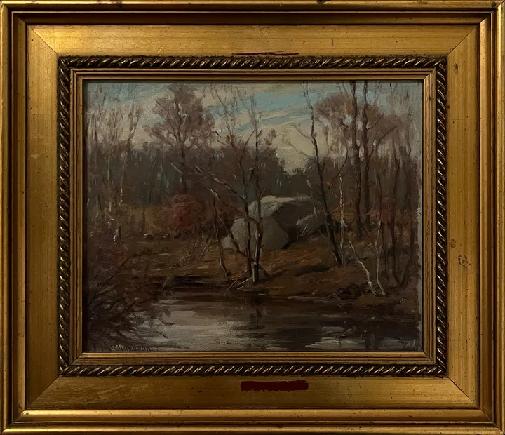 Bare trees and boulders reflected in a dark woodland pond